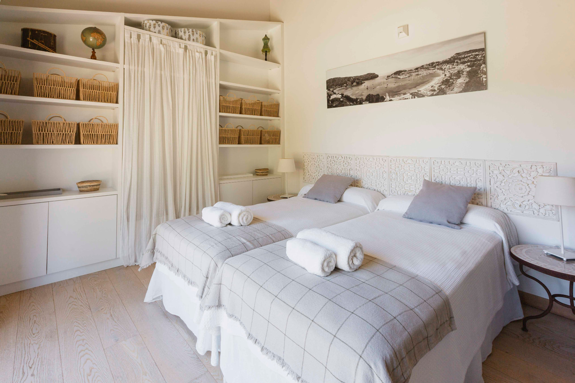 A bright twin bedroom with white linens and a sea view on the wall